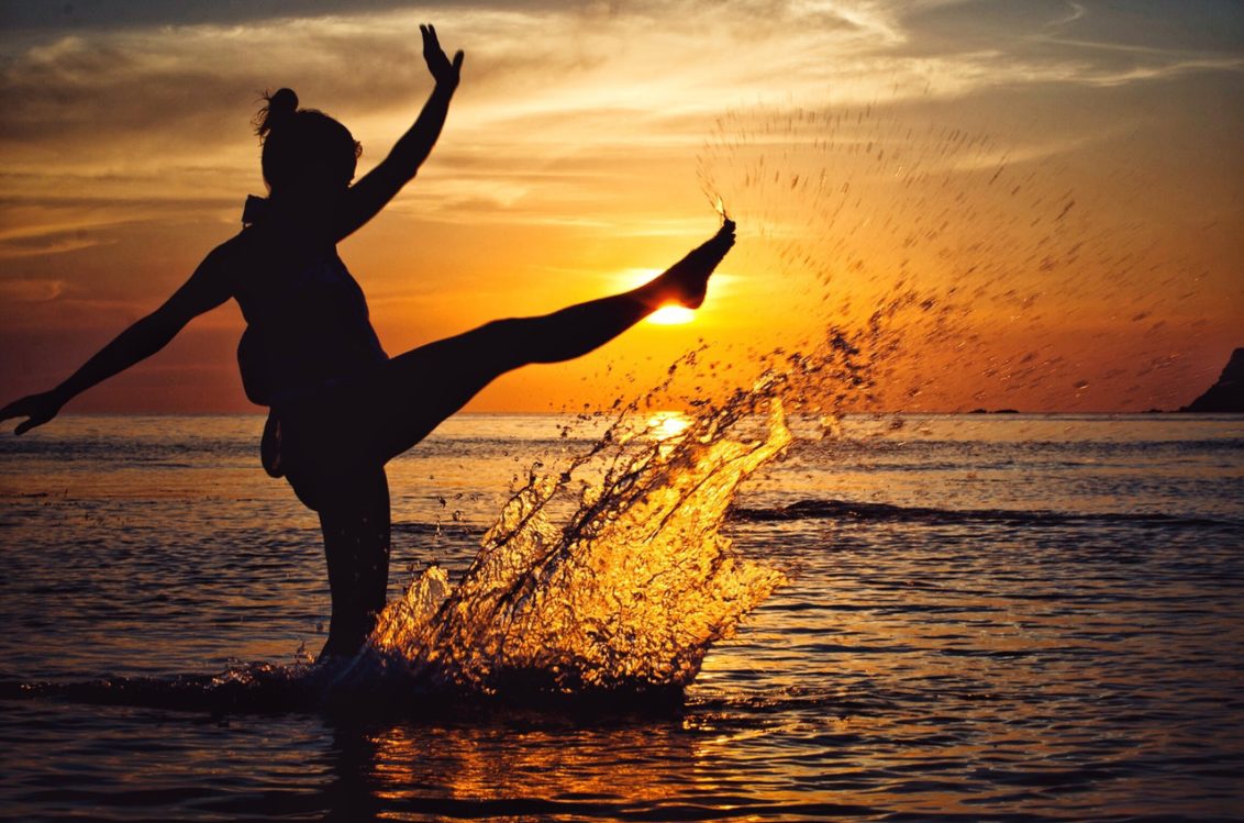 A silhouetted woman in the sea, joyfully kicking up water